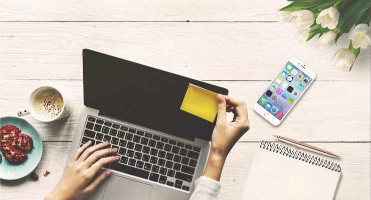 Laptop, telefon, karteczka, notes, przekąska, tulipany. Na zdjęciu widoczne ręce trzymające karteczkę.