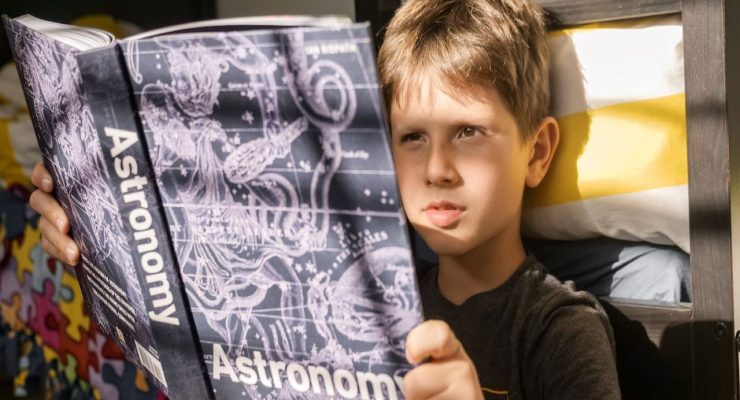 Grafika przedstawiająca chłopca czytającego książkę o astronomii.