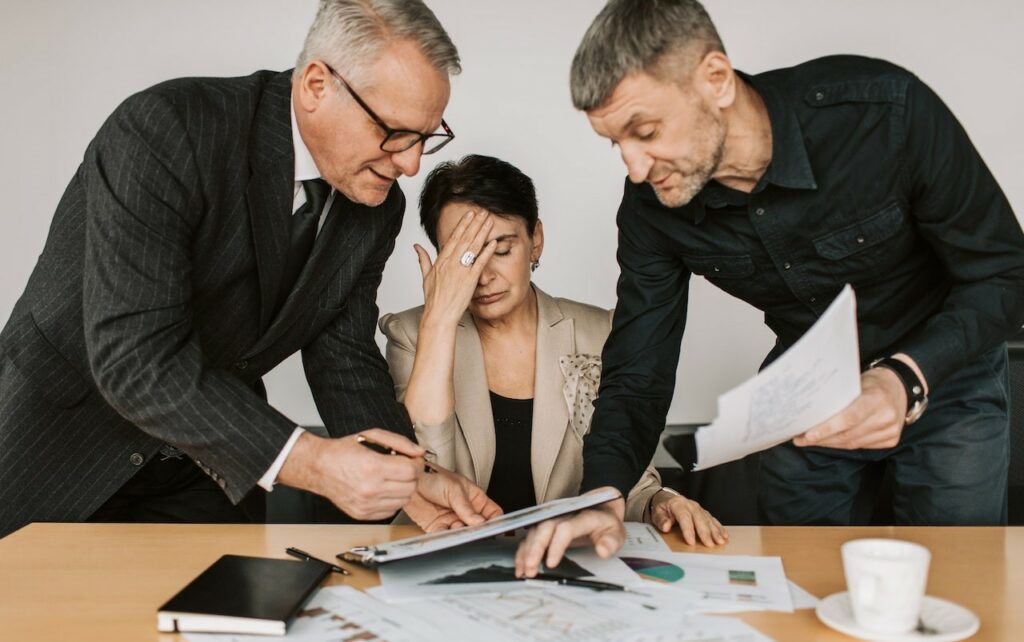 Dwóch mężczyzn przedstawiających dokumentację siedzącej kobiecie - dyrektor.