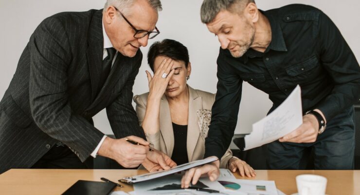 Dwóch mężczyzn przedstawiających dokumentację siedzącej kobiecie - dyrektor.