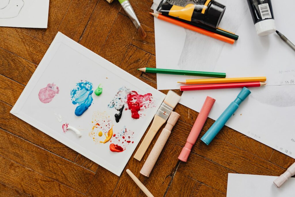 leżące na stole kredki, pisaki, kartki z dziecięcymi rysunkami