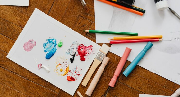 leżące na stole kredki, pisaki, kartki z dziecięcymi rysunkami