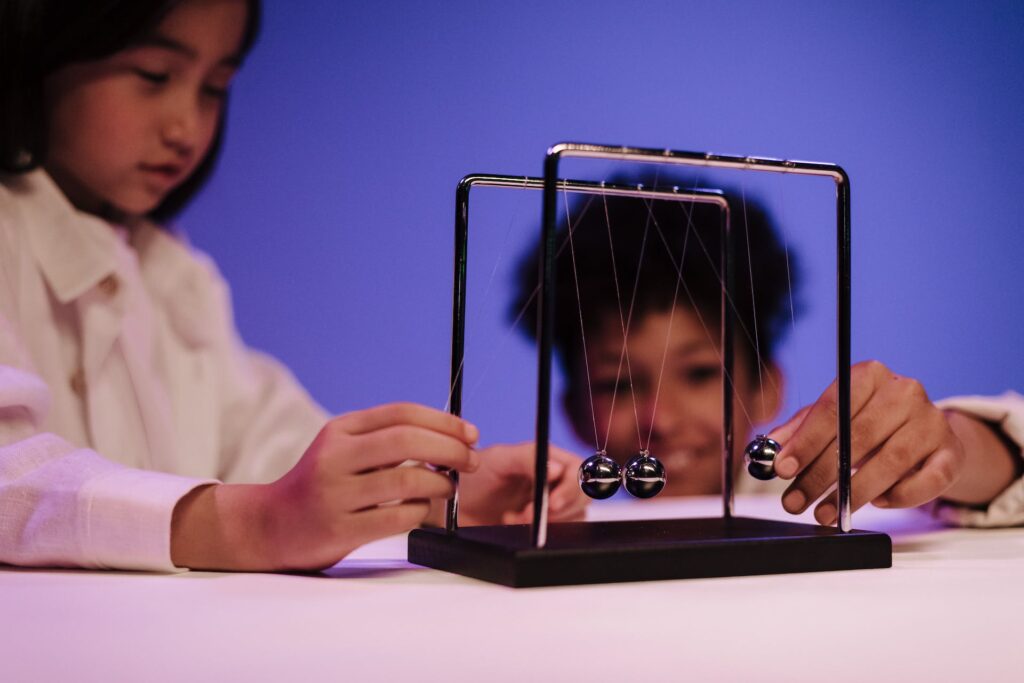 Dziewczynka i chłopiec obserwujący wahadło Newtona